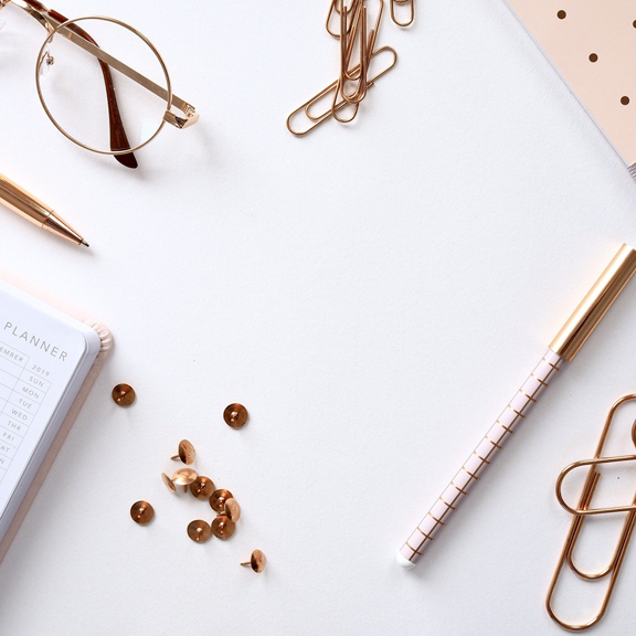 Flatlay of white desktop with pen, notebook, thumbnails, and paperclips.